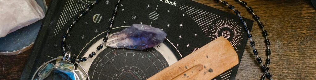 Astrology-themed flat lay featuring a birthdate book, crystals, and necklace on a wooden surface.