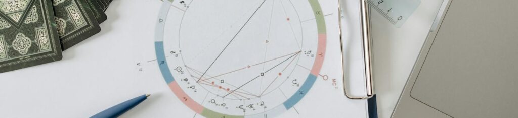 Flat lay of astrology tools, including tarot cards and a natal chart, on a desk.