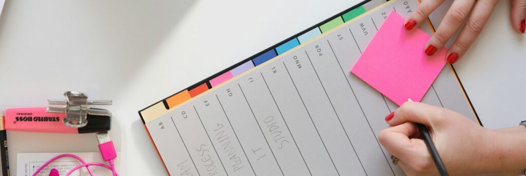person holding pencil and stick note beside table