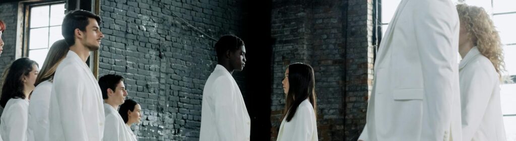 A diverse group in white suits face each other in an industrial setting, symbolizing equality.