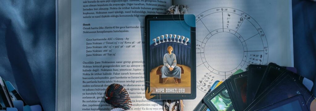 An artistic flat lay of tarot cards and astrology on a book with seashells, featuring Kupa Dokuzlusu card.