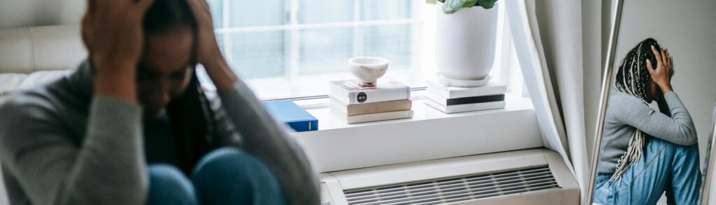 Frustrated young female having mental problem reflecting in mirror while sitting alone in room