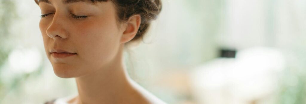 Woman with closed eyes meditating indoors, symbolizing tranquility and focus.