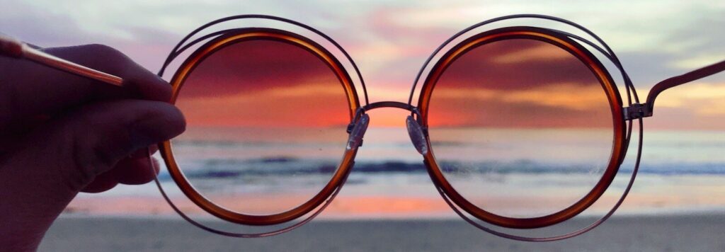 a person holding up a pair of sunglasses on the beach