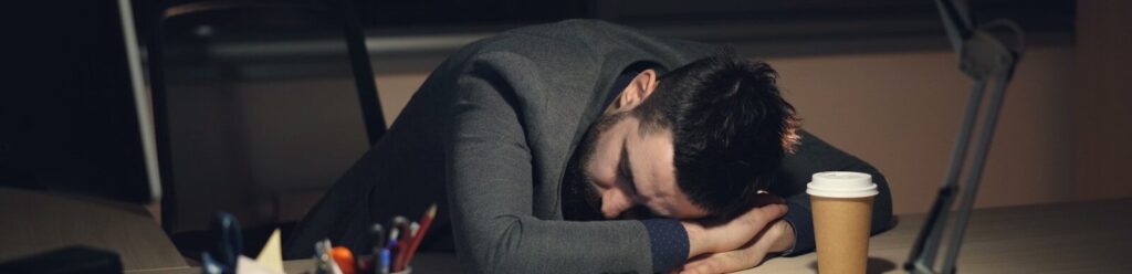 Man sleeping at desk with coffee and tablet.