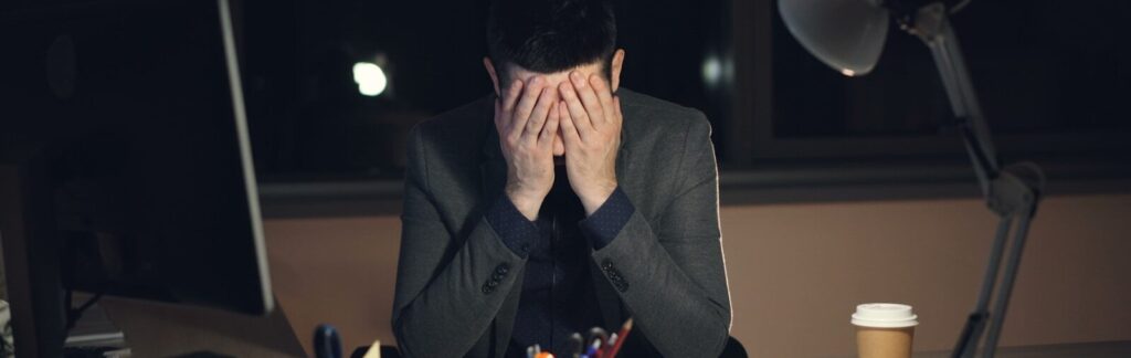 Man in suit sits at desk, head in hands.