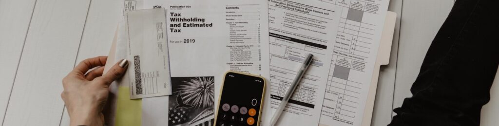 person holding paper near pen and calculator