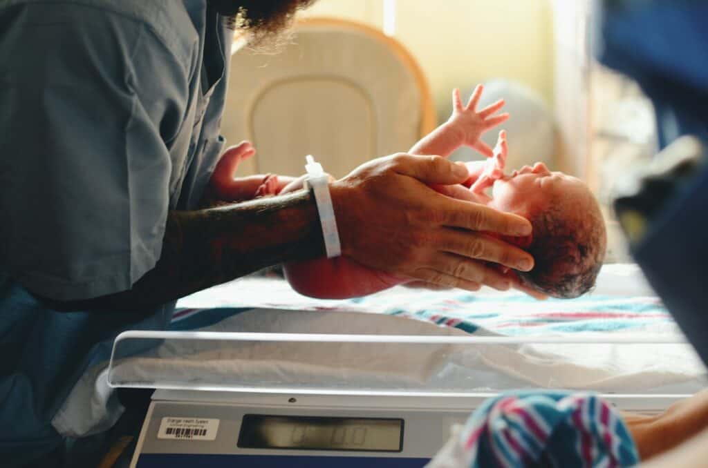 person wearing gray shirt putting baby on scale birth chart