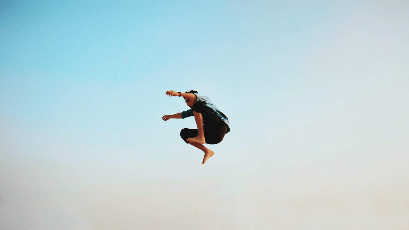 Rising sign. A man energetically jumps midair with a clear blue sky backdrop, capturing a sense of freedom.