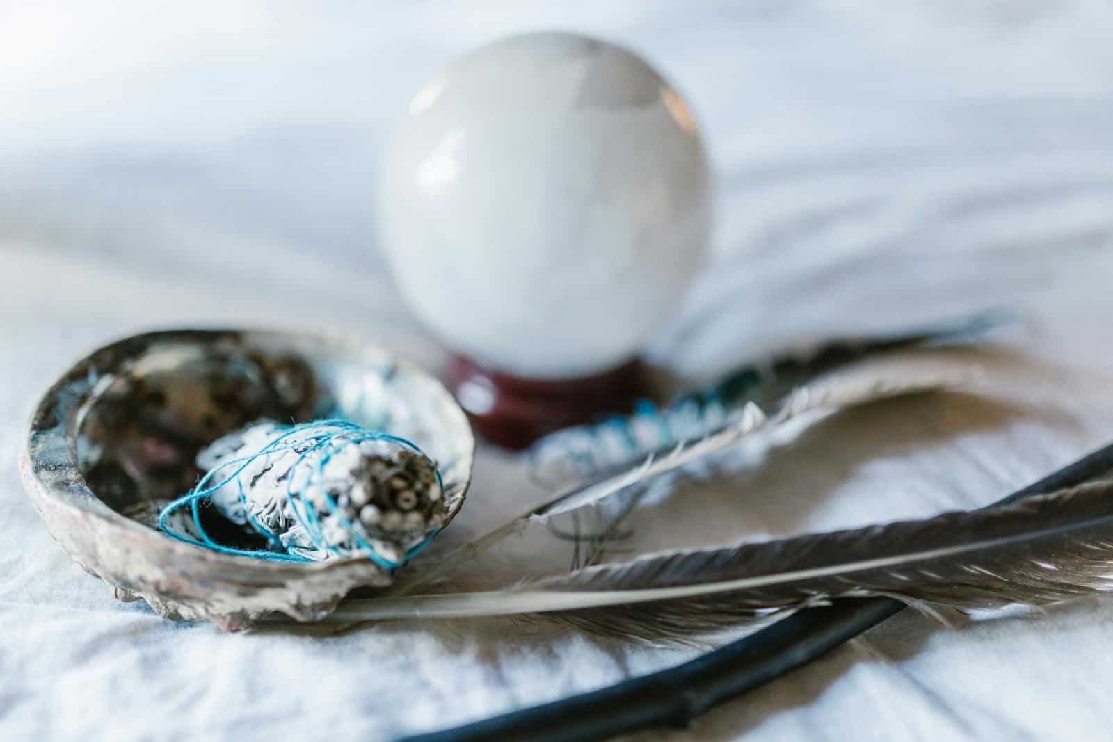 A spiritual arrangement featuring a crystal ball, sage bundle, and feathers, ideal for mystical themes. Horoscope Insights