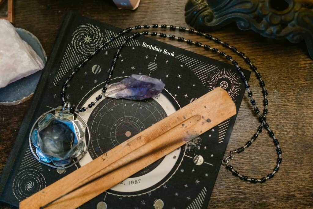 Astrology-themed flat lay featuring a birthdate book, crystals, and necklace on a wooden surface. Astrology Signs