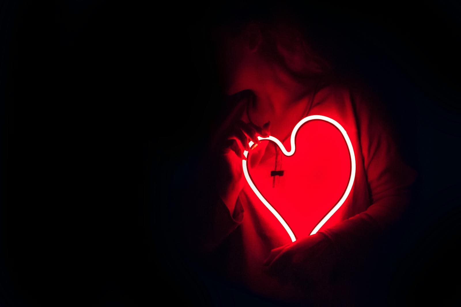 Silhouette of a person with a glowing red neon heart in the dark, symbolizing love. Zodiac Signs