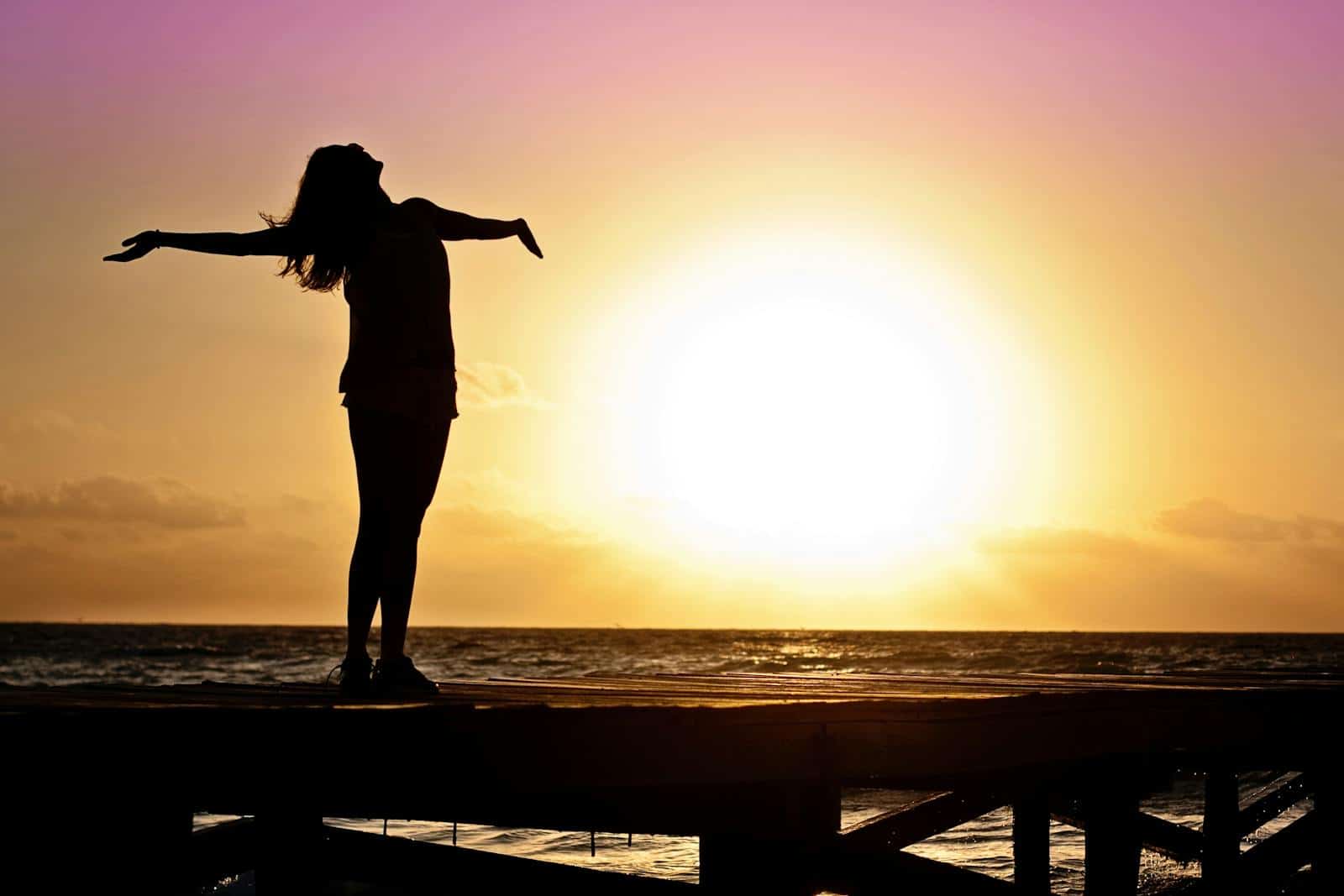 Astrology and Self-Discovery, A joyful silhouette of a woman standing on a dock at sunset, embracing the freedom of nature.