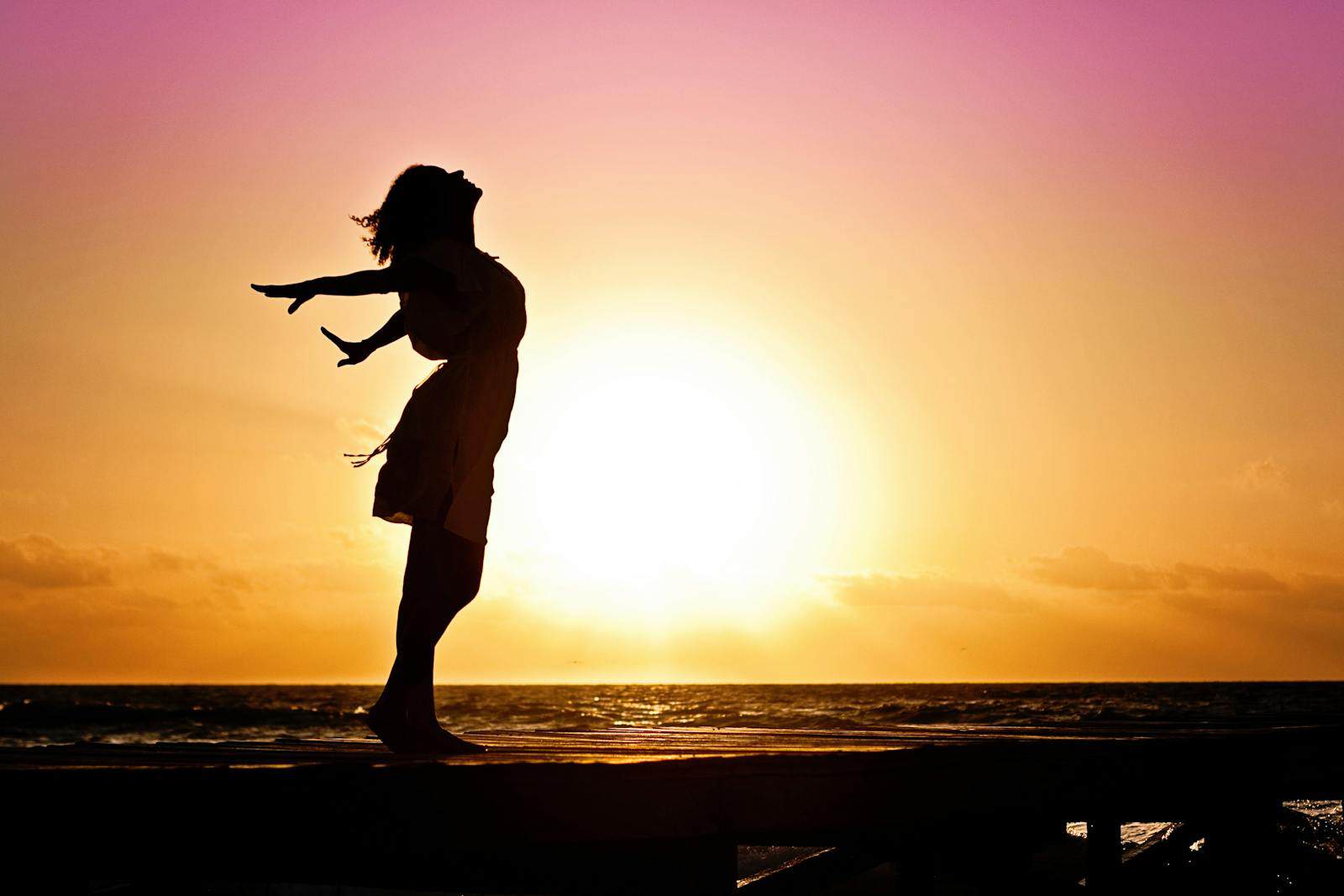 Birth Chart, Astrology, Star Gazer, Silhouette of a woman at the beach with arms outstretched against a vibrant sunset backdrop.