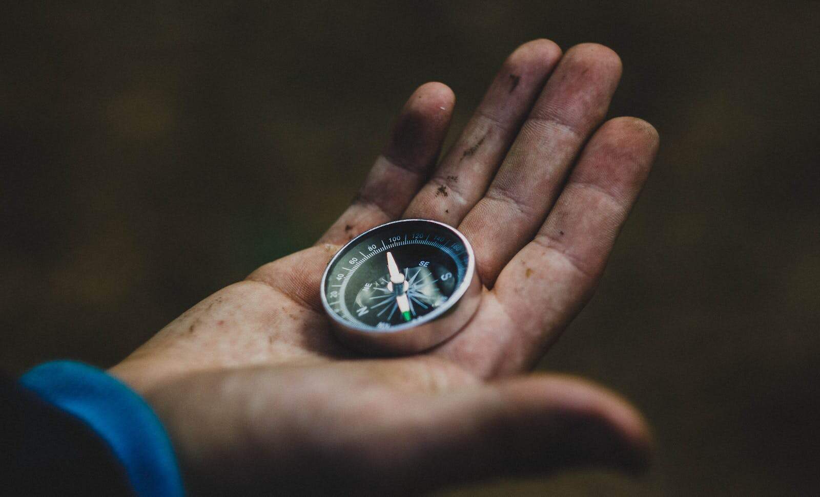 Cosmic Path, Astrology, A close-up of a compass held in a dirty hand, symbolizing adventure and navigation.