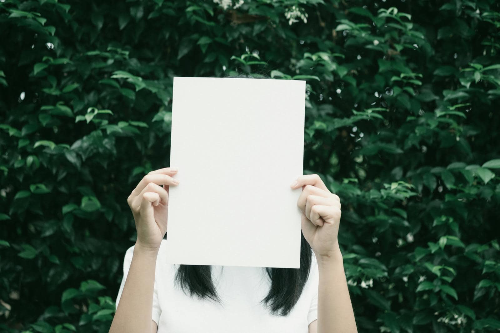Rising signs, astrology, horoscope, tarot, zodiac, A person holding a blank piece of paper in front of a lush leafy background.