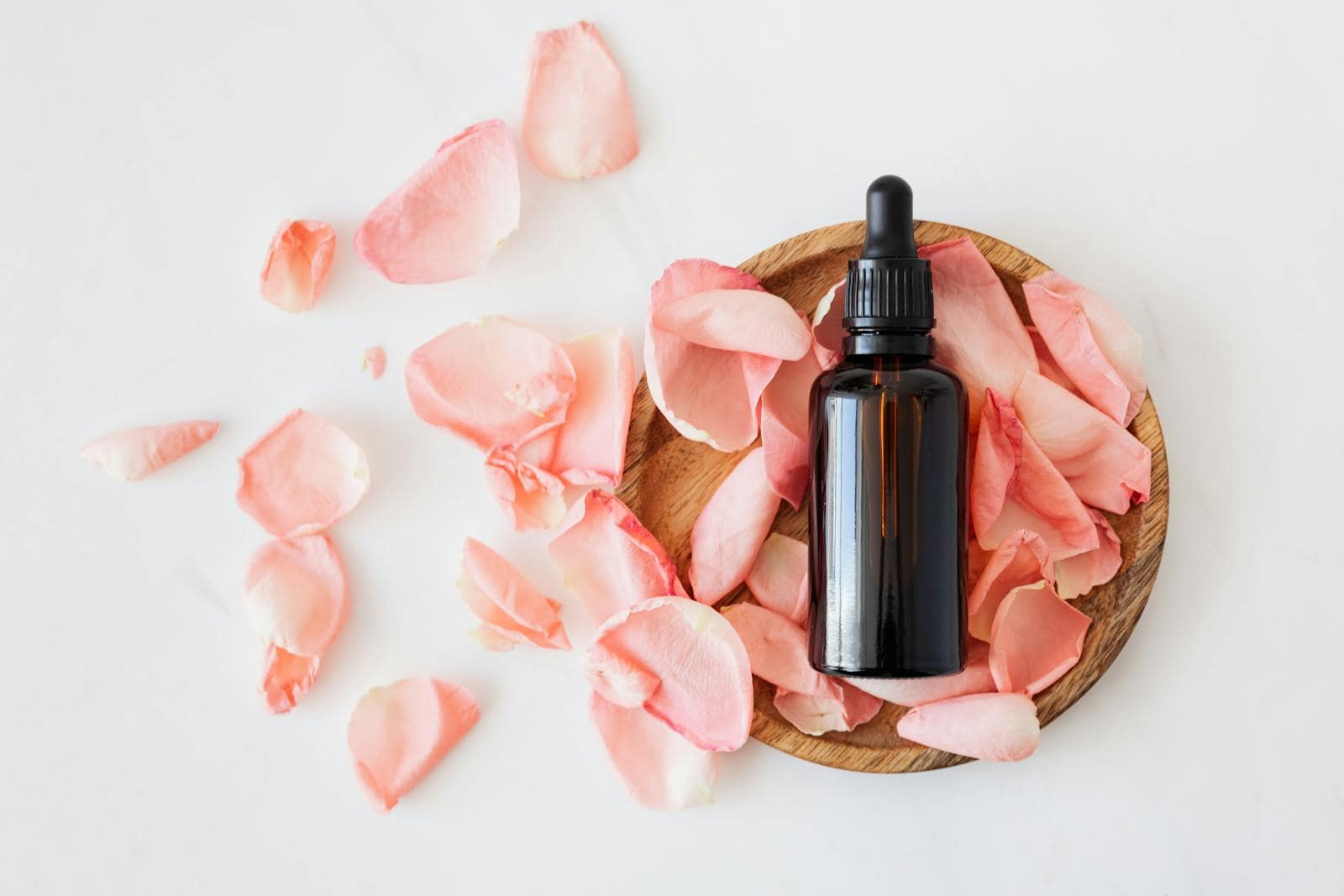 Naturopathic medicine, Top view of empty brown bottle for skin care product placed on wooden plate with fresh pink rose petals on white background isolated