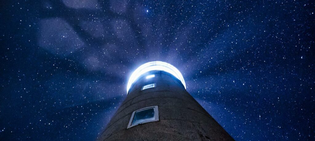 A lighthouse beam cuts through the starry night sky, casting light rays under a celestial dome, *Names have been changed for confidentiality