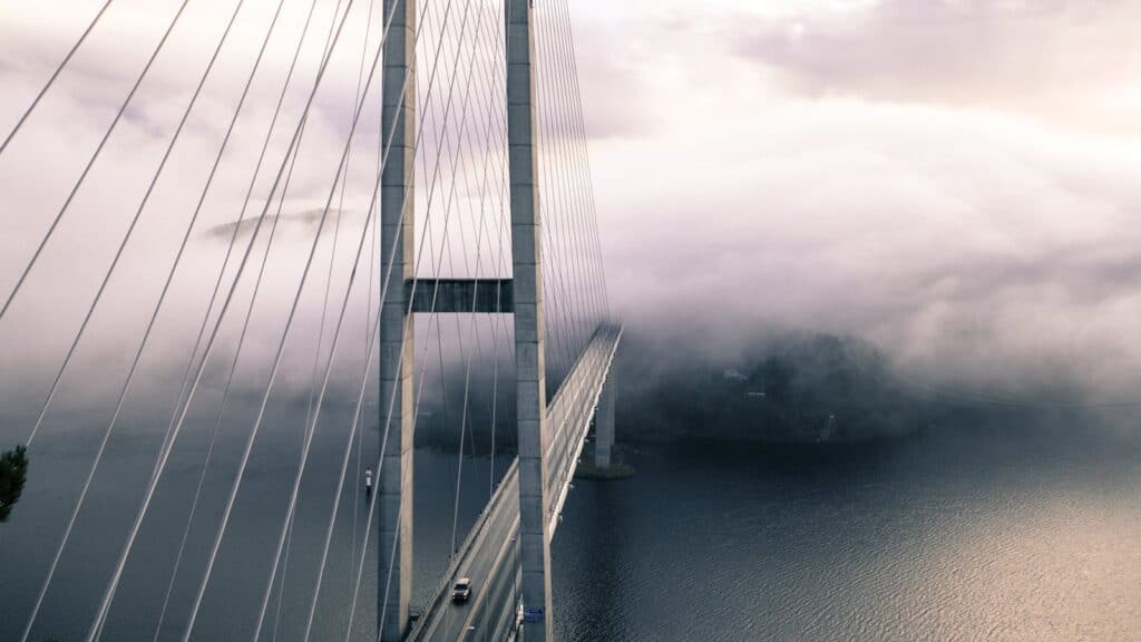 A dramatic view of a fog-covered suspension bridge with cables and the ocean below. bridge, astrology, birth chart