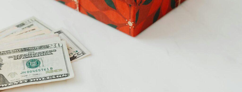 Red wrapped gift box alongside U.S. dollar banknotes on a white background.