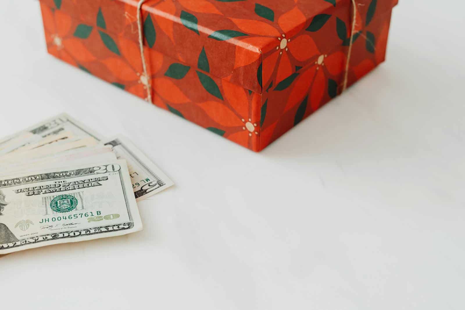 Red wrapped gift box alongside U.S. dollar banknotes on a white background. finances, zodiac, astrology, spending habits