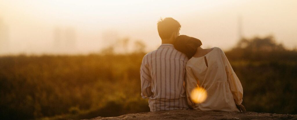 A couple enjoys a serene moment together during a sunset in Gia Lai, Vietnam. Close-up of hands holding 'Los Amantes' tarot card on a striped cloth background. Astrology birth date natal chart..