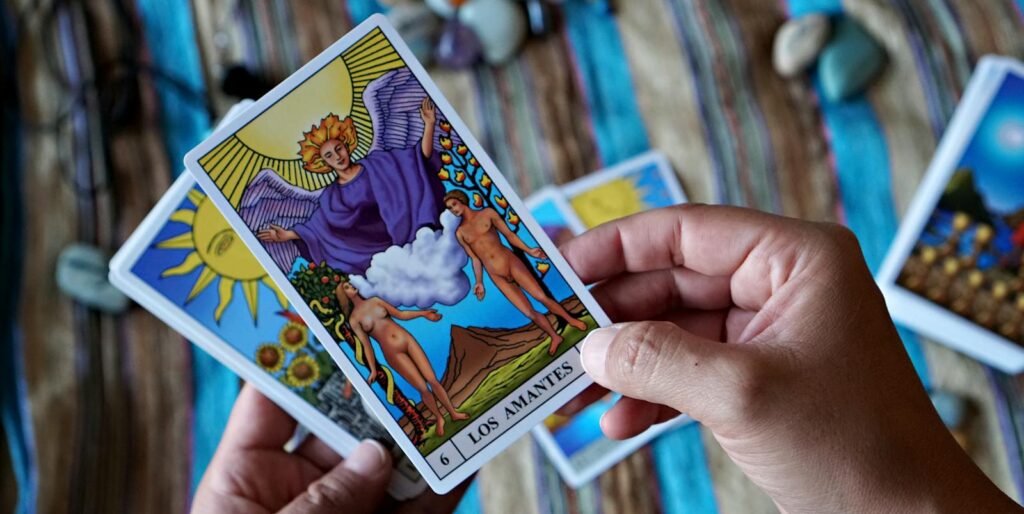 Close-up of hands holding 'Los Amantes' tarot card on a striped cloth background. Astrology birth date natal chart..