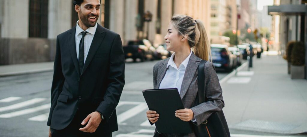 A man and woman in business attire walking across a city street, engaged in conversation. Career journey, cosmic blueprint,