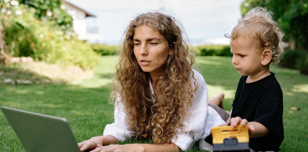 Woman working on a laptop while lying on grass with her child nearby playing. Career Jyotish Natal Chart