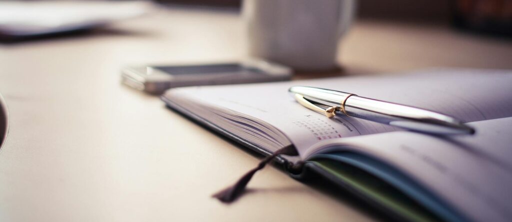 Cozy workspace with an open planner, pen, and coffee mug on a desk.