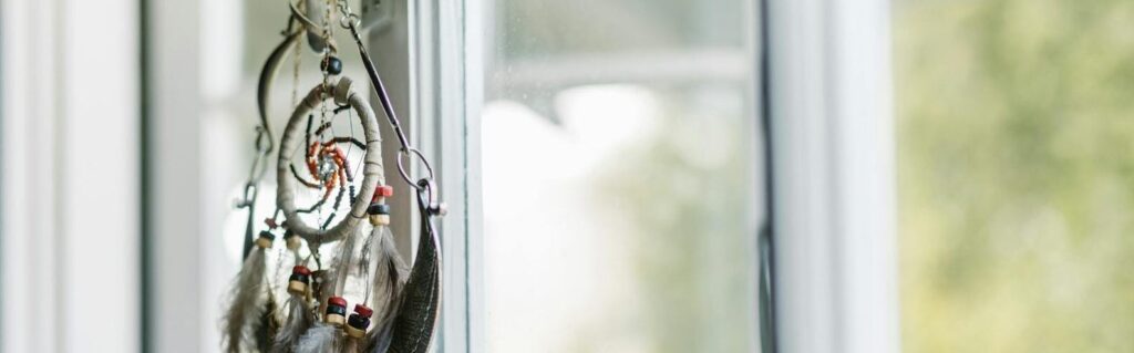 A dreamcatcher with feathers hangs by a sunlit window, creating a serene ambiance. Dreams, astrology, moon cycles