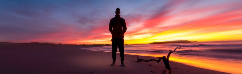 man standing on a beach during sunset