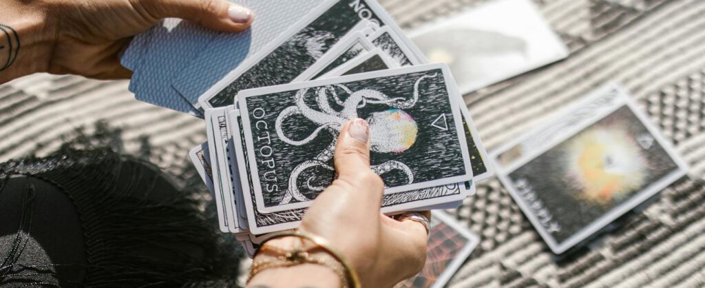 Hands holding tarot cards during a reading session on a patterned mat.