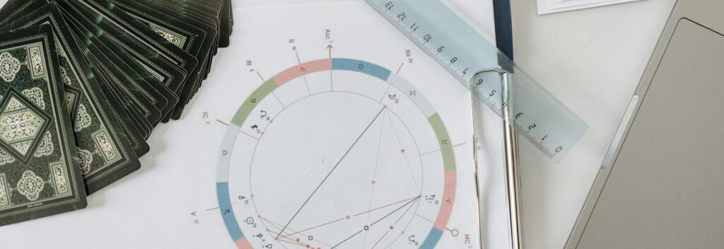 Flat lay of astrology tools, including tarot cards and a natal chart, on a desk.