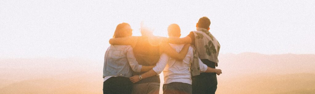 four person hands wrap around shoulders while looking at sunset