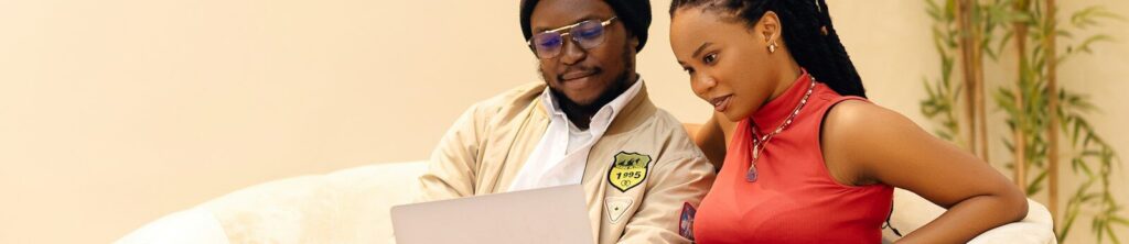 A man and a woman sitting on a couch looking at a laptop
