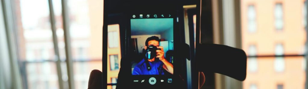 A man takes a smartphone selfie capturing his own reflection in an indoor urban setting.